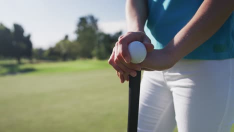 Caucasian-female-golf-player-holding-a-ball-and-a-golf-club-standing-on-golf-field