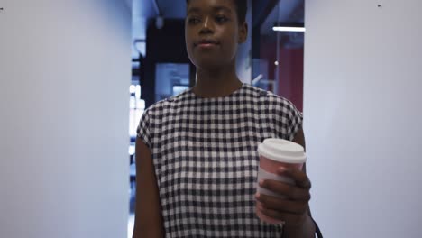Afroamerikanische-Geschäftsfrau-Mit-Kaffeetasse,-Die-Im-Büroflur-Spaziert