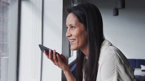 Smiling-mixed-race-businesswoman-standing-talking-on-smartphone-in-office
