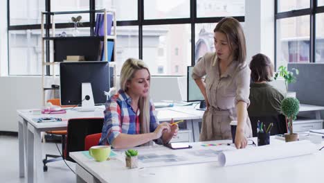 Diverse-female-office-colleagues-discussing-over-blueprint-plan-at-modern-office