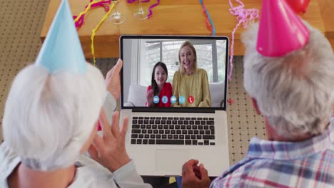 Caucasian-senior-couple-on-laptop-video-chat-wearing-party-hats-at-home