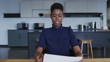 African-american-businesswoman-having-video-chat-going-through-paperwork-in-workplace-kitchen