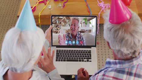 Caucasian-senior-couple-on-laptop-video-chat-wearing-party-hats-at-home