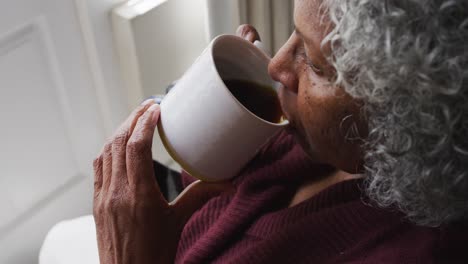 Close-up-of-senior-african-american-woman-sitting-on-the-wheelchair-drinking-coffee-at-home