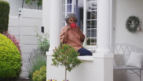 Mujer-Afroamericana-Mayor-Tomando-Café-Mientras-Está-Sentada-En-El-Porche-De-La-Casa