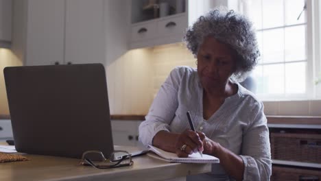 Ältere-Afroamerikanische-Frau-Benutzt-Laptop-Und-Macht-Sich-Zu-Hause-Notizen