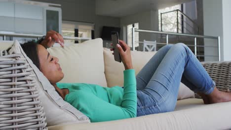 Frau-Mit-Gemischter-Abstammung-Liegt-Auf-Der-Couch-Und-Führt-Einen-Video-Chat-Auf-Dem-Smartphone,-Der-Küsse-Austeilt