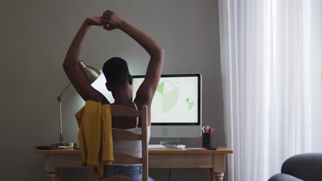 Rear-view-of-african-american-woman-stretching-her-arms-using-computer-while-working-from-home