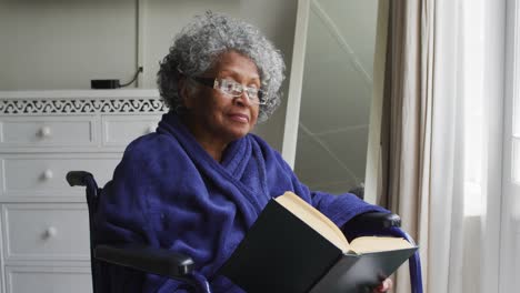 Senior-african-american-woman-sitting-on-the-wheelchair-reading-a-book-at-home