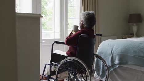 Senior-african-american-woman-sitting-on-the-wheelchair-drinking-coffee-at-home