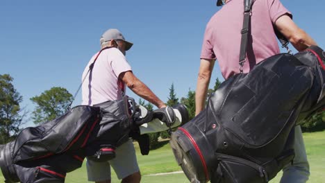 Zwei-Kaukasische-ältere-Männer-Mit-Gesichtsmasken-Gehen-Mit-Ihren-Golftaschen-Auf-Dem-Golfplatz