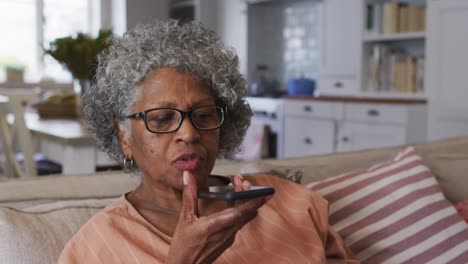 Ältere-Afroamerikanische-Frau-Spricht-Auf-Dem-Smartphone,-Während-Sie-Zu-Hause-Auf-Der-Couch-Sitzt