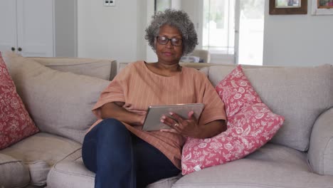 Mujer-Afroamericana-Senior-Usando-Tableta-Digital-Mientras-Está-Sentada-En-El-Sofá-En-Casa