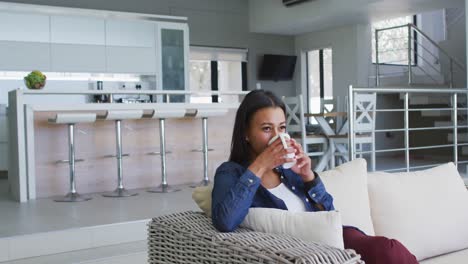 Mixed-race-woman-sitting-on-couch-drinking-cup-of-coffee