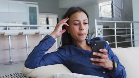 Mixed-race-woman-sittin-on-couch-having-video-chat-on-smartphone-laughing