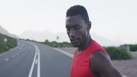 Portrait-of-african-american-man-exercising-on-mountain-road-stopping-to-rest-during-run