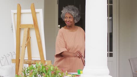 Senior-african-american-woman-painting-while-standing-on-the-porch-of-the-house