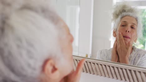 Caucasian-senior-woman-touching-her-face-while-looking-in-the-mirror-at-home