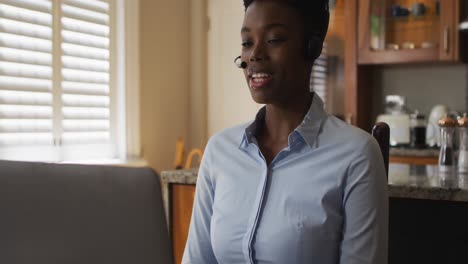 Afroamerikanische-Frau-Trägt-Ein-Telefon-Headset-Und-Führt-Einen-Videoanruf-Auf-Dem-Laptop,-Während-Sie-Von-Zu-Hause-Aus-Arbeitet