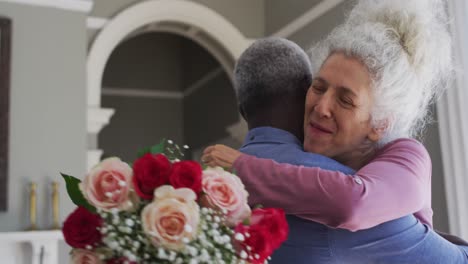 Mixed-race-senior-couple-hugging-each-other-in-the-living-room-at-home