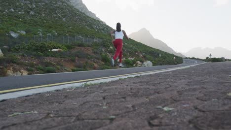 Fit-mixed-race-woman-exercising-running-on-a-country-road-near-mountains
