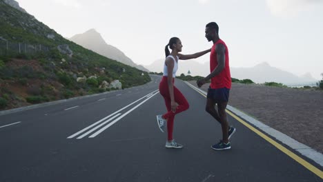 Diverse-fit-couple-exercising-stretching-on-a-country-road-near-mountains