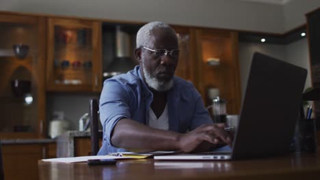 African-american-senior-man-using-laptop-and-calculating-finances-at-home