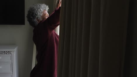 Ältere-Afroamerikanische-Frau,-Die-Zu-Hause-Die-Vorhänge-Des-Fensters-öffnet