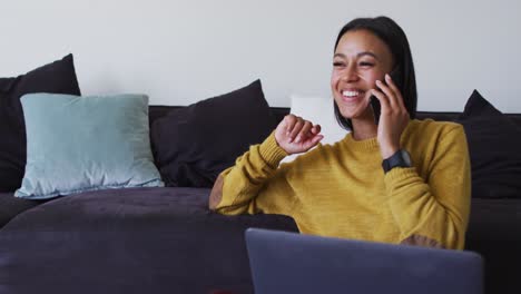Mixed-race-woman-sitting-on-floor-using-laptop-talking-on-smartphone
