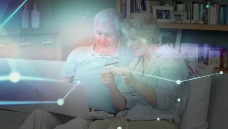 Glowing-network-of-connections-against-senior-caucasian-couple-holding-credit-card-using-laptop