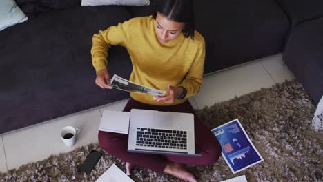 Mixed-race-woman-sitting-on-floor-using-laptop-going-through-paperwork