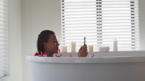 Afroamerikanische-Frau-Benutzt-Smartphone-In-Der-Badewanne-Im-Badezimmer-Zu-Hause
