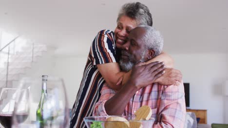 African-american-senior-couple-sitting-by-a-table-drinking-wine-eating-dinner-and-hugging