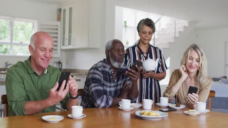 Zwei-Unterschiedliche-Seniorenpaare-Sitzen-Zu-Hause-An-Einem-Tisch-Und-Trinken-Tee-Mit-Smartphones