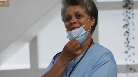 Portrait-of-senior-african-american-female-doctor-wearing-face-mask-looking-at-camera-and-smiling