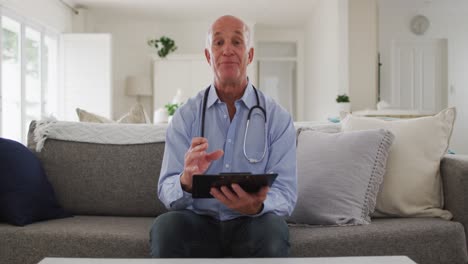 Senior-caucasian-male-doctor-giving-video-call-consultation-from-home-using-tablet-computer