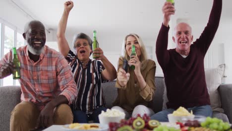 Two-diverse-senior-couples-sitting-on-a-couch-watching-a-game-drinking-beer