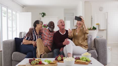 Two-diverse-senior-couples-sitting-on-a-couch-using-a-smartphone-and-laughing