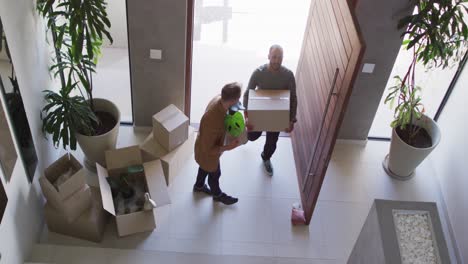 Multi-ethnic-gay-male-couple-walking-through-carrying-packing-boxes-in-to-house