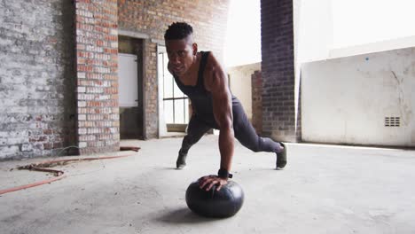 African-american-man-exercising-doing-push-ups-on-medicine-ball-in-an-empty-urban-building