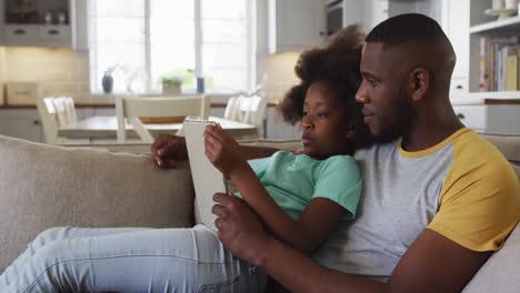 Hija-Afroamericana-Y-Su-Padre-Usando-Una-Tableta-Juntos-Sentados-En-El-Sofá