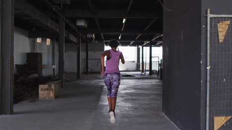 Mujer-Afroamericana-Vistiendo-Ropa-Deportiva-Corriendo-Por-Un-Edificio-Urbano-Vacío