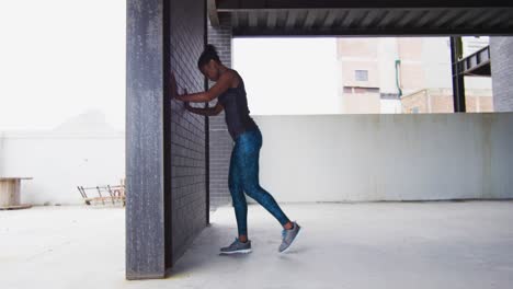African-american-woman-stretching-leaning-on-a-wall-in-an-empty-urban-building