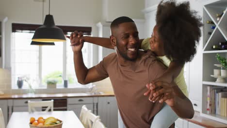 African-american-daughter-on-her-father's-back-embracing-him-in-kitchen