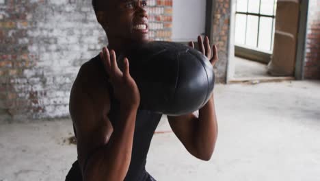 Hemdloser-Afroamerikanischer-Mann,-Der-In-Einem-Leeren-Städtischen-Gebäude-Mit-Einem-Medizinball-Trainiert