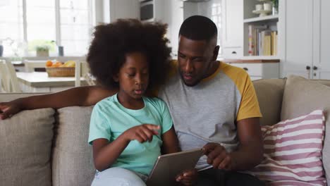 Hija-Afroamericana-Y-Su-Padre-Usando-Una-Tableta-Juntos-Sentados-En-El-Sofá