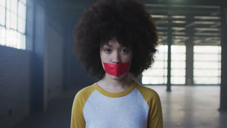 Portrait-of-african-american-woman-with-red-tape-on-her-mouth-in-empty-parking-garage