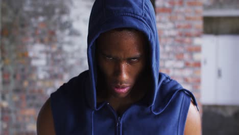 Portrait-of-african-american-man-wearing-hoodie-sweating-after-exercise-looking-at-camera-in-urban-b