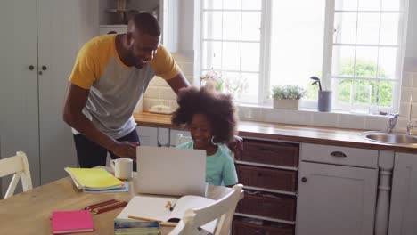 Hija-Afroamericana-Y-Su-Padre-Usando-Una-Computadora-Portátil-Juntos-En-La-Mesa-De-La-Cocina