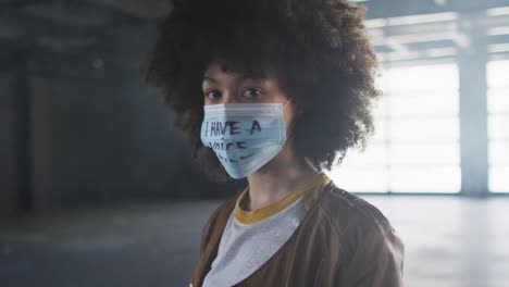Portrait-of-african-american-woman-wearing-protest-face-mask-in-empty-parking-garage